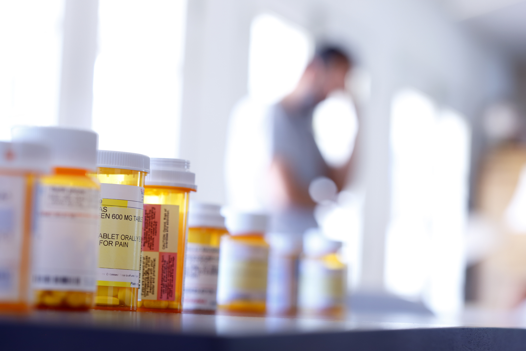 close up of pill bottles with person standing blurry in background