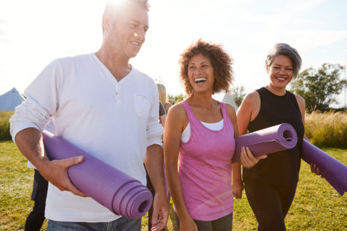 Group Of Mature Men And Women With Exercise Mats At End Of Outdoor Yoga Class